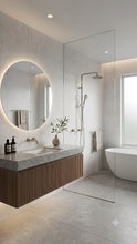 Load image into Gallery viewer, Modern bathroom interior with a floating vanity, round backlit mirror, glass shower enclosure, freestanding tub, and light stone surfaces.