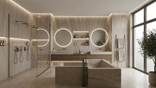 Load image into Gallery viewer, A modern luxury bathroom interior featuring a stone double vanity with illuminated round mirrors, a glass shower enclosure, a rectangular stone bathtub, and a large window with a potted plant.
